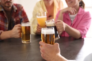 Friends with glasses of beer at grey table indoors, selective focus
