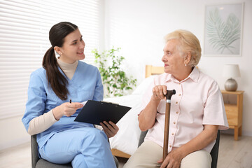 Obraz premium Nurse with clipboard examining senior woman indoors. Home health care service