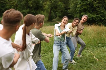 Fototapeta premium Team building. Group of happy people playing tug of war with rope outdoors