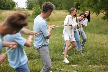 Fototapeta premium Team building. Group of happy people playing tug of war with rope outdoors