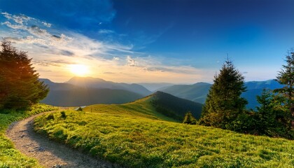 Obraz premium a bright sunrise over a grassy hilltop with scattered trees and a winding path overlooking distant blue mountains beneath a partly cloudy sky