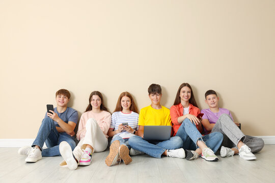 Group of teenagers with laptop and smartphones near beige wall indoors. Space for text