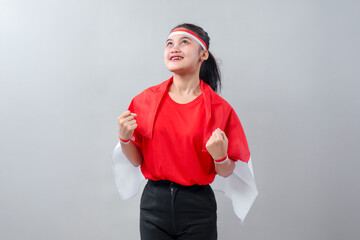 Optimistic Indonesian girl in red and white outfit stands proud, looking up with joy and clenched...