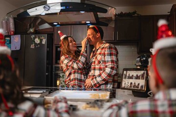 Couple in matching pajamas laughing and baking Christmas cookies in kitchen
