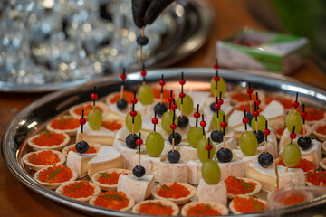 Elegant catering platter with gourmet appetizers: red caviar tartlets, brie cheese cubes topped with grapes and blueberries on skewers. Perfect for event, party, or luxury food stock content.