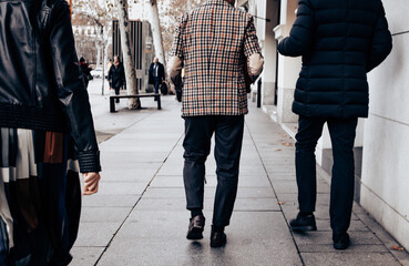 Stylish people walk down a city sidewalk on a cold day, showcasing fashion on a city sidewalk. One...
