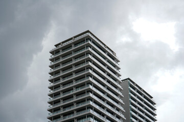 Fototapeta premium Contemporary high-rise building with numerous glass windows and balconies, gray sky background, urban architecture, clean lines and geometric shapes.