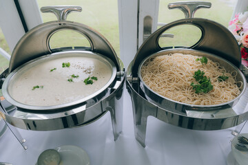 Buffet of Culinary Delights: A close-up shot showcasing a delectable buffet spread featuring two chafing dishes, one brimming with creamy soup and the other with a tempting noodle dish.