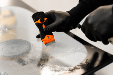 Technician uses scraper to clean the surface of a new windshield post-replacement. Technician...