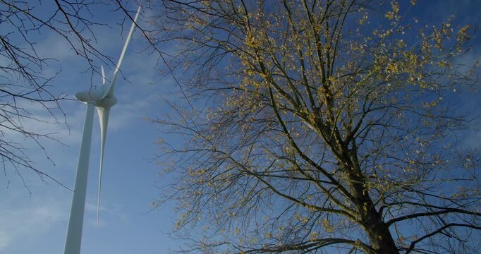 Wind turbine windmill turning in a blue sky with clouds and trees