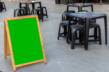 Empty green chroma key for mockup sandwich chalkboard next to tables and chairs and a food truck in a square in Brazil