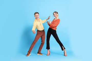 Happy couple in retro outfits dancing on light blue background