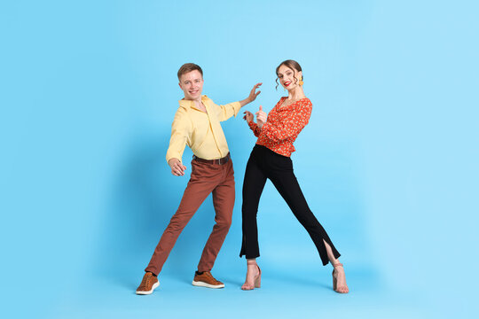 Happy couple in retro outfits dancing on light blue background - Powered by Adobe