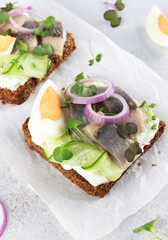 Danish smorrebrod with herring, egg, cucumber, onion on rye bread on white background. Close up