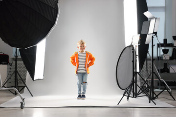 Little boy on light grey background in photo studio with professional equipment