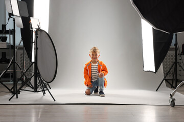 Little boy on light grey background in photo studio with professional equipment