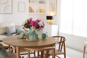 Dining table with beautiful flowers and dishware in room. Interior design