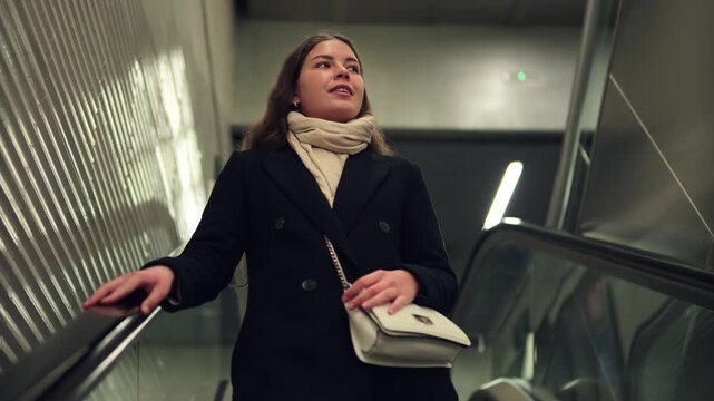 A determined young woman rides the escalator with confidence, looking ahead as she navigates through a busy transportation hub, embodying the spirit of modern commuting and the daily journey of