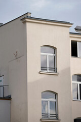 Residential building facade with smooth plaster walls, arched windows, metal railings, reflective glass, minimalistic exterior, showing light architectural wear in soft daylight.


