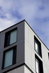 Facade corner of a modern building featuring black and white panels with large tinted windows. The sharp contrast between panels and reflective glass creates a minimalist architectural statement.

