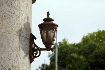Antique wall lantern with ornate metalwork and frosted glass mounted on textured stone. The vintage...