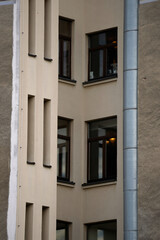 Detailed view of beige building corner with dark brown framed windows. Vertical grooves on the facade add architectural depth, with visible interior lighting through clean glass panes.

