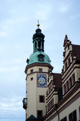 Fototapeta premium Historic clock tower with ornate details and a verdigris copper roof stands tall against a cloudy sky, featuring a large, intricate clock face with Roman numerals and decorative elements.