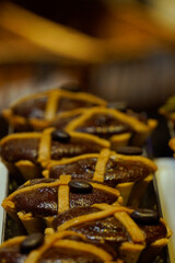 Rich chocolate tarts with golden pastry crusts topped with coffee beans and crushed pistachios are arranged neatly in metal trays, showcasing glossy textures and artisanal baking craftsmanship.

