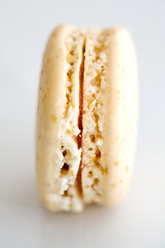An elegant close-up of a vanilla macaron with a delicate, crisp shell and smooth filling. Set against a minimal white background, the image emphasizes the texture and fine details