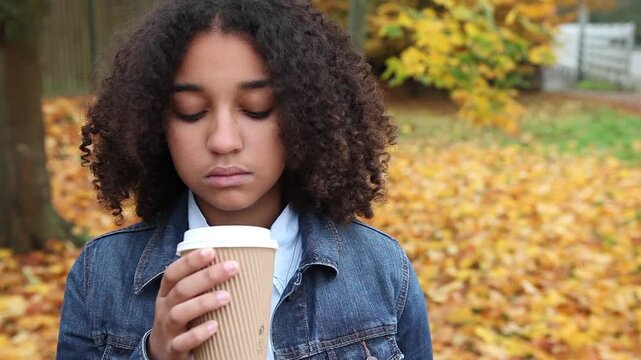 Beautiful mixed race African American girl teenager young woman wearing a blue denim jacket outside sad or depressed then happy smiling drinking coffee or tea