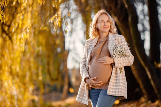 Caucasian mature pregnant woman standing in autumn park - Powered by Adobe