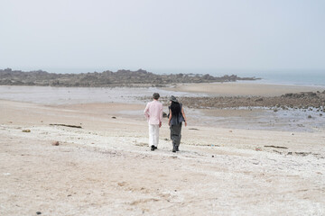 In June 2025, a Korean man and woman in their late fifties walk along the peaceful seashore,...