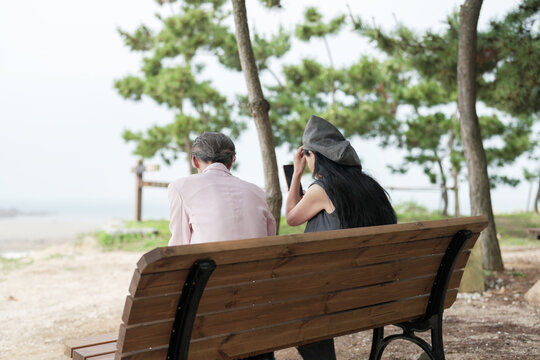In June 2025, a Korean man and woman in their late fifties sit on a bench by the sea, chatting and smiling as they enjoy the breeze, ocean view, and calm surroundings in Incheon Metropolitan City.