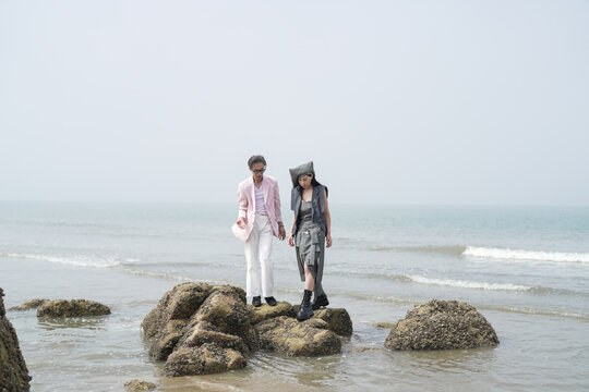 In June 2025, a Korean man and woman in their late fifties are playing together along the rocky shoreline, stepping over jagged stones and enjoying the coastal scenery in Incheon Metropolitan City.