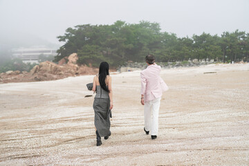 In June 2025, a Korean man and woman in their late fifties walk along the peaceful seashore,...