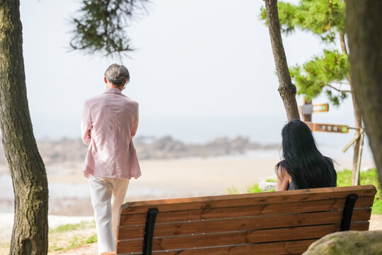 In June 2025, a Korean man and woman in their late fifties sit on a bench by the sea, chatting and smiling as they enjoy the breeze, ocean view, and calm surroundings in Incheon Metropolitan City.