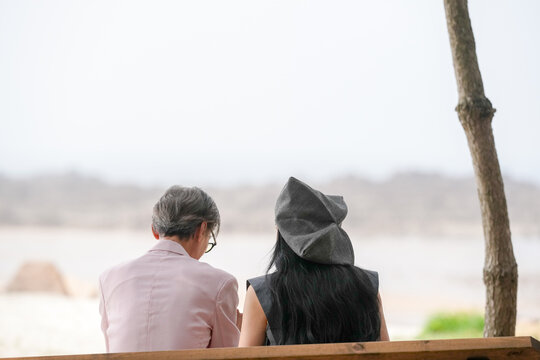 In June 2025, a Korean man and woman in their late fifties sit on a bench by the sea, chatting and smiling as they enjoy the breeze, ocean view, and calm surroundings in Incheon Metropolitan City.