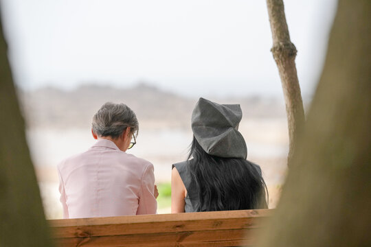 In June 2025, a Korean man and woman in their late fifties sit on a bench by the sea, chatting and smiling as they enjoy the breeze, ocean view, and calm surroundings in Incheon Metropolitan City. - Powered by Adobe