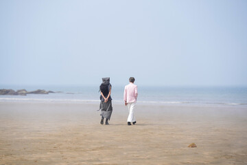 In June 2025, a Korean man and woman in their late fifties walk along the peaceful seashore, enjoying the soft ocean breeze, quiet moments, and each other's company in Incheon Metropolitan City.