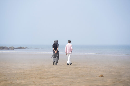 In June 2025, a Korean man and woman in their late fifties walk along the peaceful seashore, enjoying the soft ocean breeze, quiet moments, and each other's company in Incheon Metropolitan City.