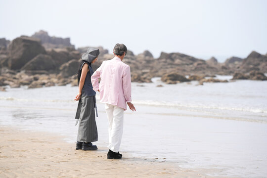 In June 2025, a Korean man and woman in their late fifties are standing and talking beside the rugged shoreline filled with jagged rocks and crashing waves in Incheon Metropolitan City, South Korea.