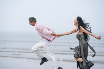 In June 2025, a Korean man and woman in their late fifties are running at full speed along the rugged shoreline filled with jagged rocks and crashing waves in Incheon Metropolitan City, South Korea.