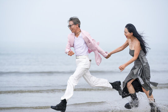 In June 2025, a Korean man and woman in their late fifties are running at full speed along the rugged shoreline filled with jagged rocks and crashing waves in Incheon Metropolitan City, South Korea. - Powered by Adobe