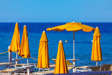 Bright yellow beach umbrellas stand over the tranquil blue sea. Beach umbrellas stand guard over...