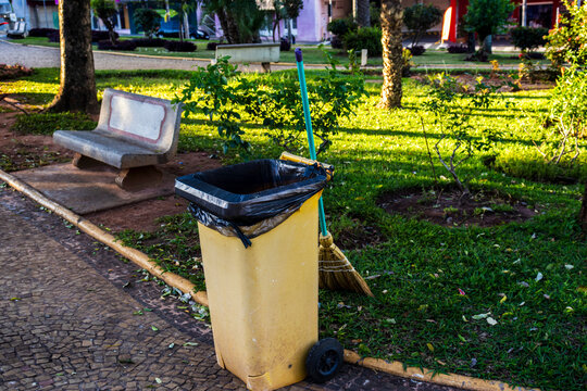 Yellow mobile trash can with straw broom in a square of a Brazilian city. Illustrates urban cleaning and waste management.