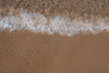 Close-up of foamy seawater gently washing onto smooth wet sand at the edge of a beach during...