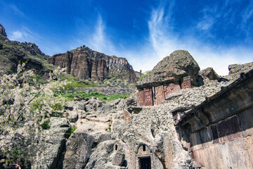 Geghard Monastery carved in rock, surrounded by basalt cliffs and blooming trees in spring, Armenia UNESCO heritage site