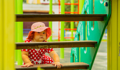 A young child is climbing through a playground structure on a sunny day Dressed in a red dress with white polka dots and a matching hat she explores with curiosity