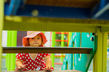 A young child is climbing through a playground structure on a sunny day Dressed in a red dress with white polka dots and a matching hat she explores with curiosity