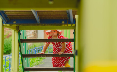 A young child is climbing through a playground structure on a sunny day Dressed in a red dress with white polka dots and a matching hat she explores with curiosity